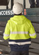 A unisex hi-vis full zip stretch taped hoodie in yellow and navy with reflective stripes, worn by a person in a hard hat.