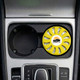 A round, yellow air freshener is placed in a car cup holder, featuring a logo and a vented design.