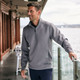A half zip jacket in grey worn by a man, standing by a railing with a waterfront view.