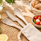A calico pouch containing biodegradable cutlery: a fork, knife, and spoon in a light beige colour, set on a woven placemat.