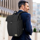 A black Osprey Arcane Flap Backpack is worn on the back of a man in a suit, standing outdoors. A black Osprey Arcane Flap Backpack is worn on the back of a man in a suit, standing outdoors.