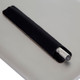 A metal pen with a silver tip, resting in a black leather holder on a grey surface. The image features branding. A metal pen with a silver tip, resting in a black leather holder on a grey surface. The image features branding.