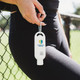 A white 50mL sunscreen bottle with a keyring attachment, held by a person in black leggings. It features a logo.