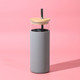 A drink bottle with a grey silicone sleeve, clear glass body, and wooden lid, featuring a reusable straw. A drink bottle with a grey silicone sleeve, clear glass body, and wooden lid, featuring a reusable straw.