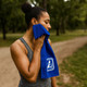 A woman in a grey tank top holds a blue cooling towel to her face, set in a green outdoor location.