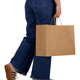 A person walking while carrying a large brown paper bag with handles. The bag is unmarked and plain.