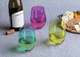 A wine bottle with three coloured glasses—green, yellow, and purple—alongside a cheese platter with crackers and cheese.