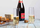 A bottle of champagne with two clear stemless flutes, set on a rustic table with cheese and snacks.