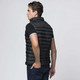 A dark black padded vest is worn by a model, featuring a high collar and fitted silhouette, with a logo visible.
