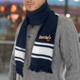 A navy and white scarf with fringed ends and a logo, worn around the neck of a person in a grey knitted jumper.