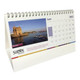 A wiro-bound tent desk calendar featuring a scenic image and a calendar grid, predominantly in white with colourful accents.