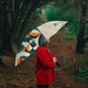 A full colour golf umbrella featuring geometric patterns, held by a person in a red jacket amidst a wooded path.