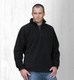 A man wearing a black polar fleece pullover with a half zip, standing against a light wooden background.