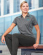 A grey polo shirt with contrast blue accents, featuring a logo, worn by a woman sitting outdoors.