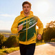 A man wearing a yellow and green men's polyester sublimated training track jacket, jogging outdoors in the sunlight.