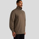 A man wearing a brown Stencil Half Zip Crew jumper, featuring a high collar and a front zip. The product has a logo.