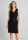 A sleeveless V-neck dress in black, featuring a fitted design and a smooth fabric. The model presents a relaxed pose.