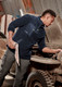 A man in a navy lightweight 1/4 zip polar fleece, working on a vehicle, with a logo on the garment.