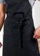 A black apron featuring a waist tie and front pockets, designed for practical workwear use.