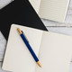 A Serenity Aluminium Pen rests on an open notebook with blank pages, accompanied by a black notebook in the background. A Serenity Aluminium Pen rests on an open notebook with blank pages, accompanied by a black notebook in the background.