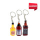 Three custom-shaped resin keychains resembling miniature bottles, featuring yellow, red, and brown colours. Each keychain has a ring attachment.
