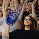 A foam hand supporter in blue and white, raised by a woman wearing sunglasses, amid an enthusiastic crowd. A foam hand supporter in blue and white, raised by a woman wearing sunglasses, amid an enthusiastic crowd.