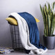 A navy blue and white blanket draped over a black wire basket with a yellow cushion and a potted plant nearby.
