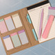 A Daily Note Planner in a kraft cover with pastel-coloured sticky notes, a pink pen, and a highlighter.