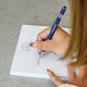 A blue metal pen with a logo is being used to write on a notepad with a decorative header.