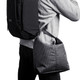 A cooler bag in a grid pattern, featuring a shoulder strap, being carried on the side of a person with a backpack.