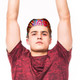 A person wearing a brightly patterned bandana, raising their arms, dressed in a red shirt. The bandana features vibrant colours.