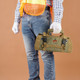 A khaki tool bag is held by a person wearing blue jeans and a safety vest, with gloves on.