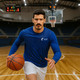 A man wearing a blue long-sleeve shirt and white shorts is dribbling a basketball on a court. The shirt has a logo.