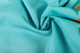 A close-up of turquoise polyester spandex fabric, showcasing its smooth texture and vibrant colour patterns.