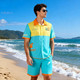 A men's button-up shirt in aqua and yellow, featuring a logo, worn on the beach with shorts.