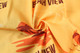 A close-up of a yellow fabric with a beach view design featuring palm trees and waves. It has a logo in the pattern.
