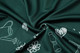 A close-up of dark green fabric featuring a pattern of white floral and gardening illustrations.