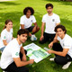 A group of five young adults wearing unisex white RPET sublimated round-collar tee shirts, sitting on grass.