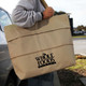 A beige, extendable shopping bag carried by a person, featuring a logo on the front.