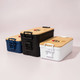 Three lunch boxes in navy, black, and white with bamboo lids and handles. All feature a logo on the top.