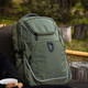 An olive green backpack sits on a chair, featuring multiple compartments and a logo.