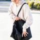 A black duffle bag with an adjustable strap, being held open by a person in a light-coloured top.