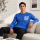 A blue unisex long-sleeve crew neck shirt with a logo, displayed on a model sitting on a sofa.