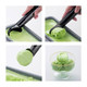 An ice cream scoop with a black handle is shown scooping green ice cream, forming a ball in a glass bowl.