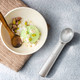 A silver ice cream scoop rests beside a bowl of green ice cream topped with nuts and garnishes.