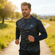 A model wearing a navy and patterned polyester spandex 1/4 zip raglan jacket while jogging outdoors.
