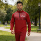 A man wearing a red 1/4 zip splicing raglan jacket with a stand-up collar, featuring a logo and white accents.