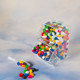 A clear dispenser filled with assorted colour mini jelly beans, with a small scoop beside it.