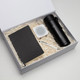 A black drink bottle, notebook, white speaker, and pen in a gift box with shredded paper filling.