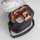 A black insulated bag with a silver interior, containing a wooden board and snacks. It has an adjustable strap.
